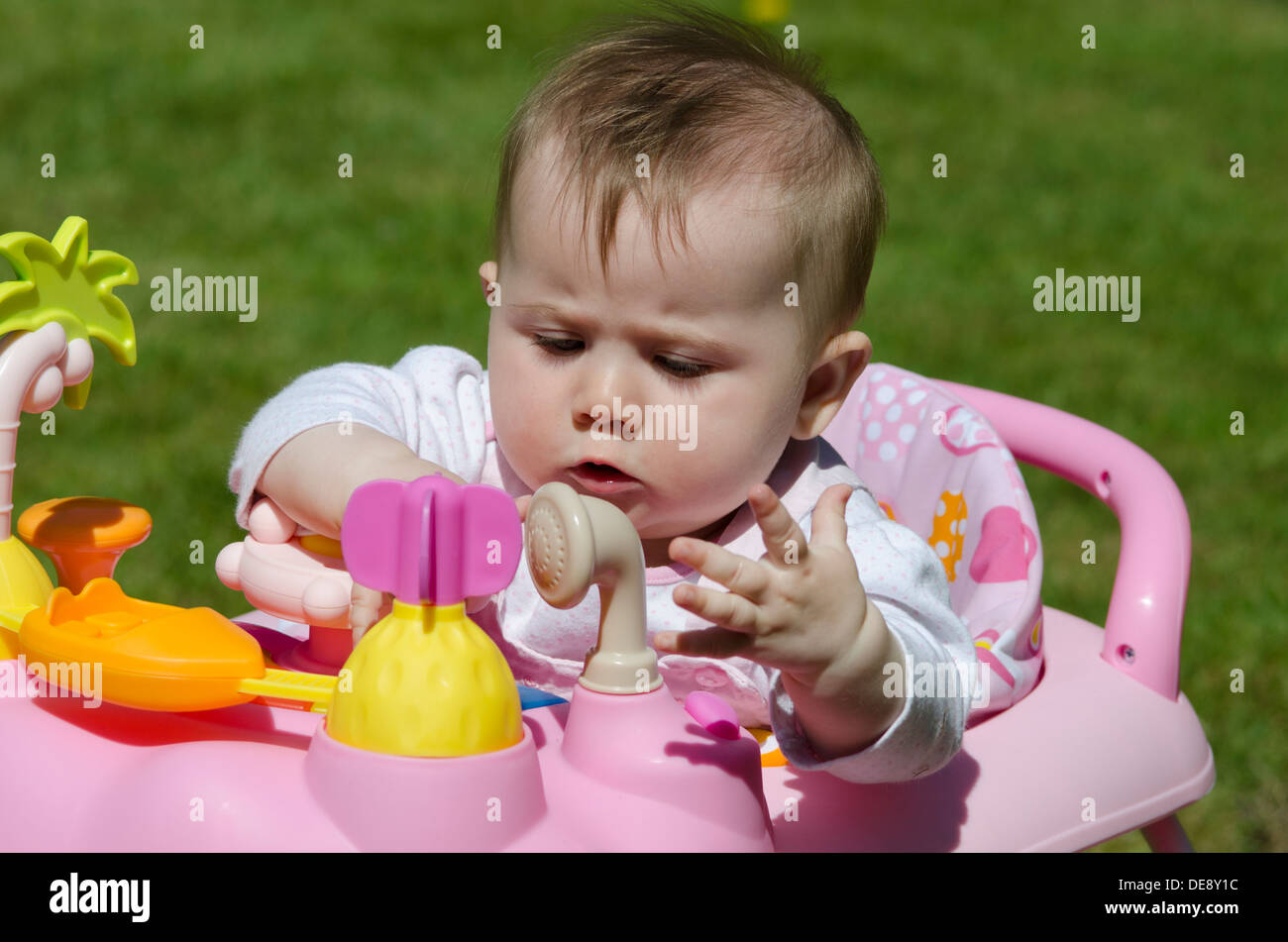 eight month old baby girl sitting in high chair with toys in garden on lawn Stock Photo