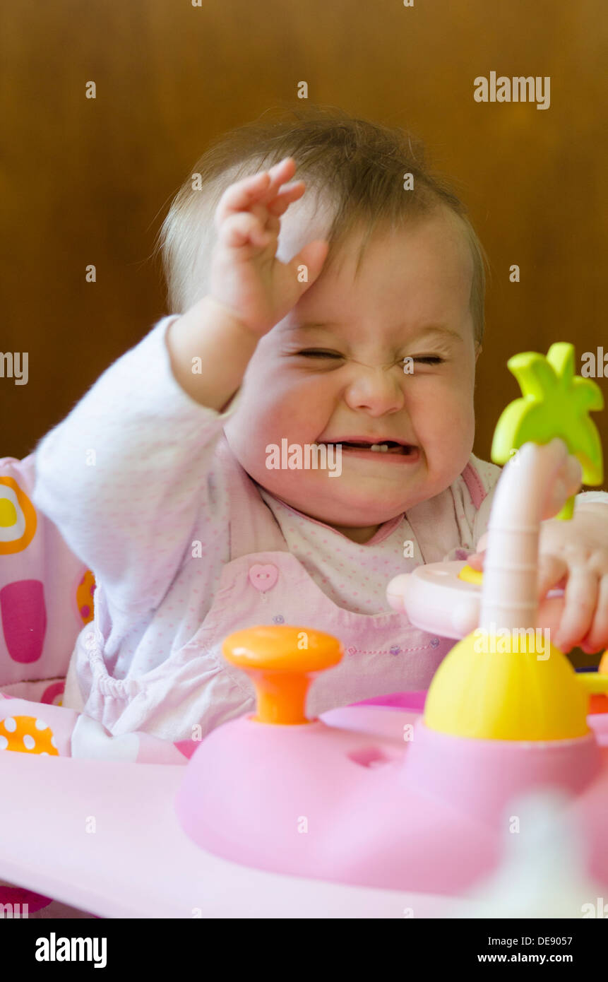 eight month old baby girl sitting in high chair with toys Stock Photo