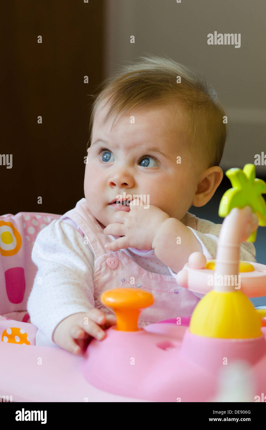 eight month old baby girl sitting in high chair with toys Stock Photo
