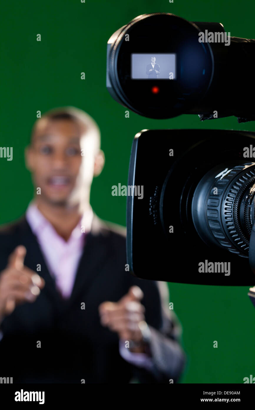 Close-up of a television camera viewfinder and lens with a presenter out of focus in the background. Stock Photo