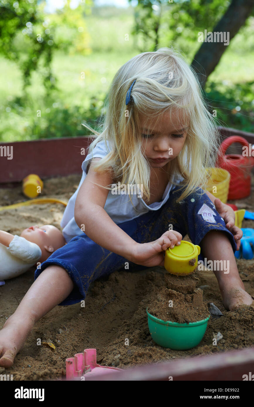 Little blond girl playing in sandpit at summer garden Stock Photo