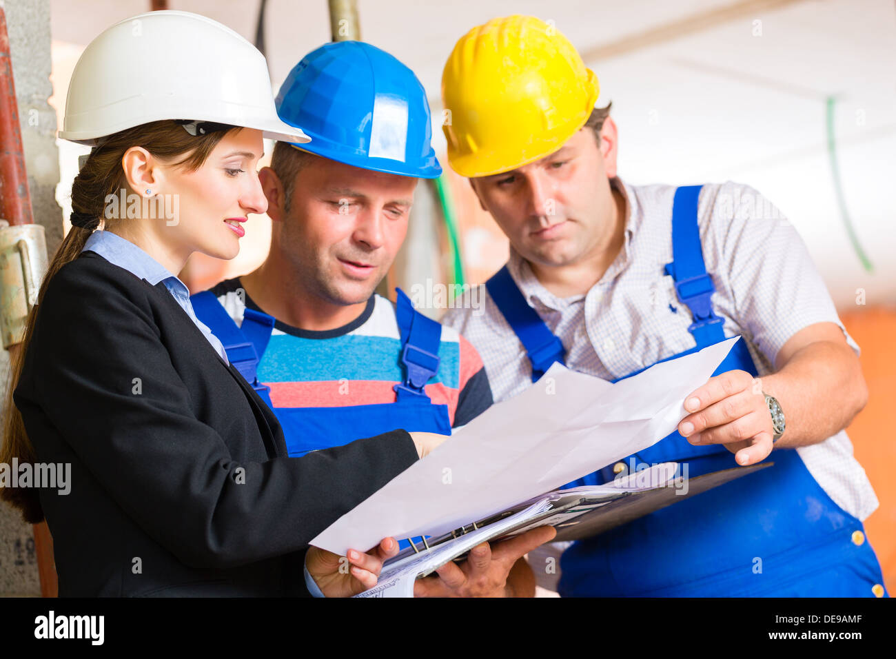 Construction site team or architect and builder or worker with helmets controlling or having discussion of plan or blueprint Stock Photo