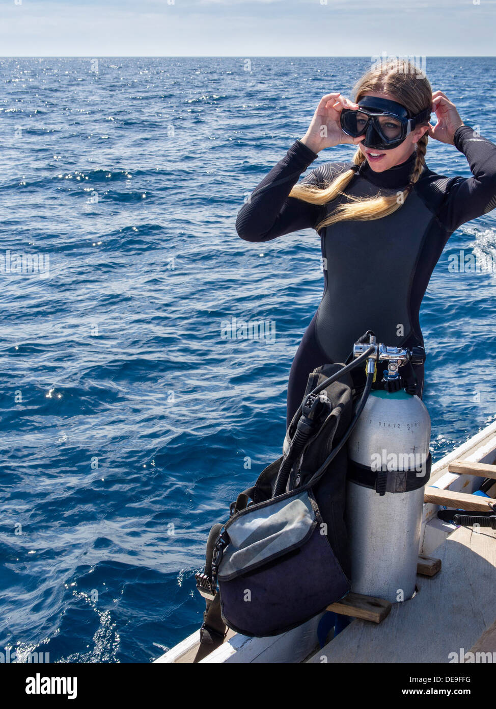 Caucasian woman on a boat in the ocean adjusts her goggles in preparation for scuba diving. Stock Photo