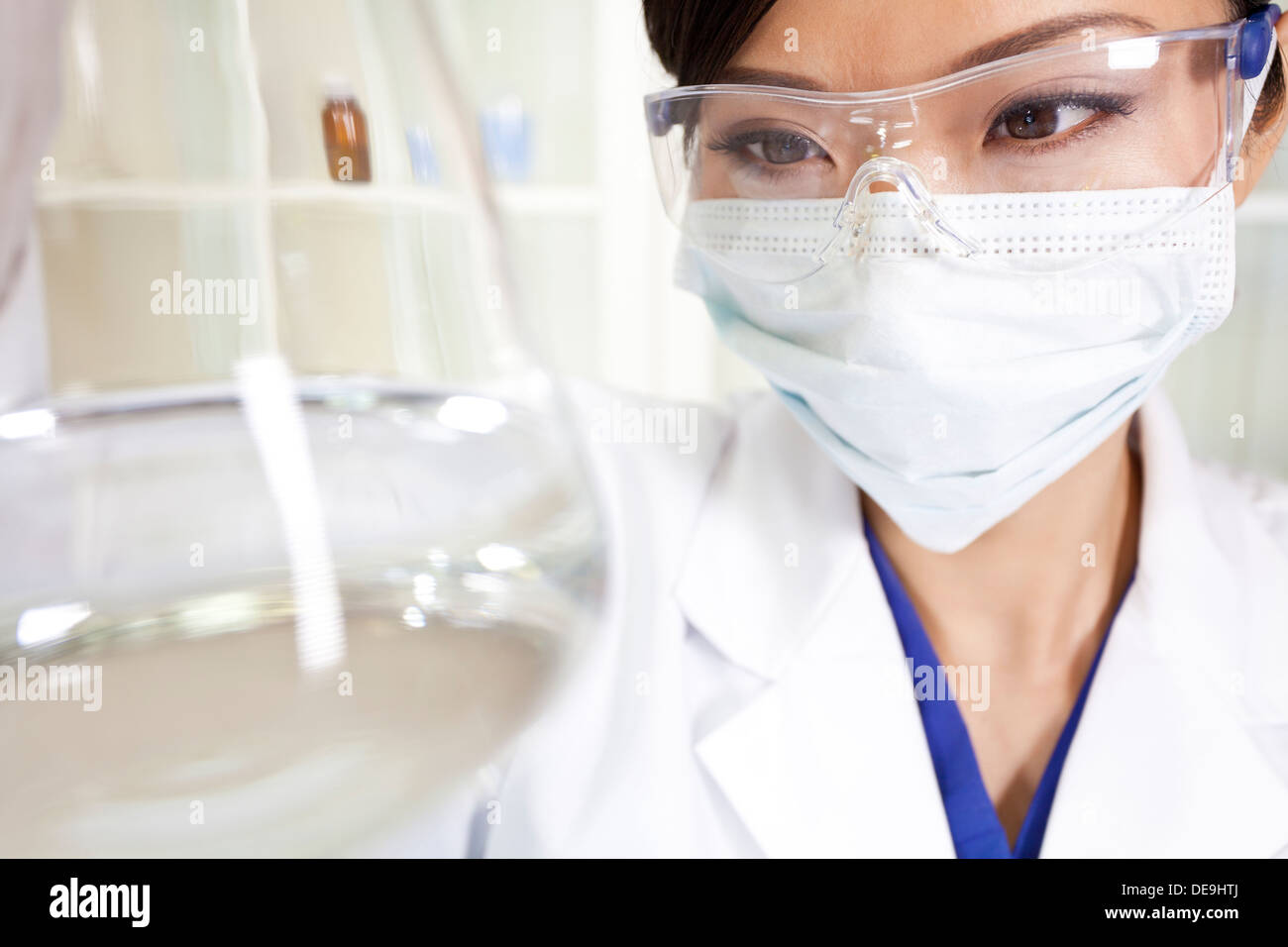 Chinese Asian female medical or scientific researcher or doctor using looking at a conical flask of clear liquid in laboratory Stock Photo