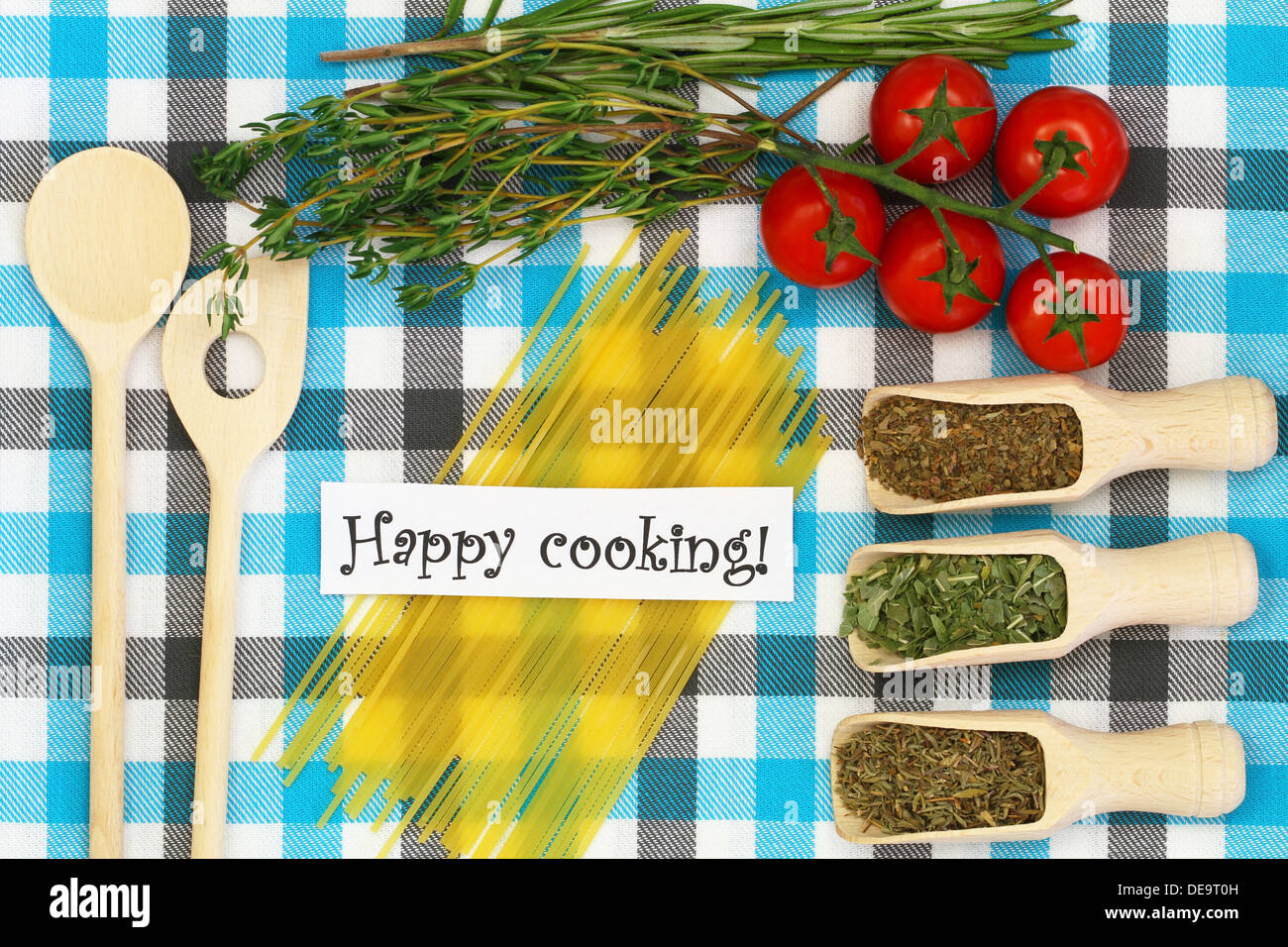 Happy cooking card with selection of herbs, ingredients and kitchen utensils on checkered tablecloth Stock Photo