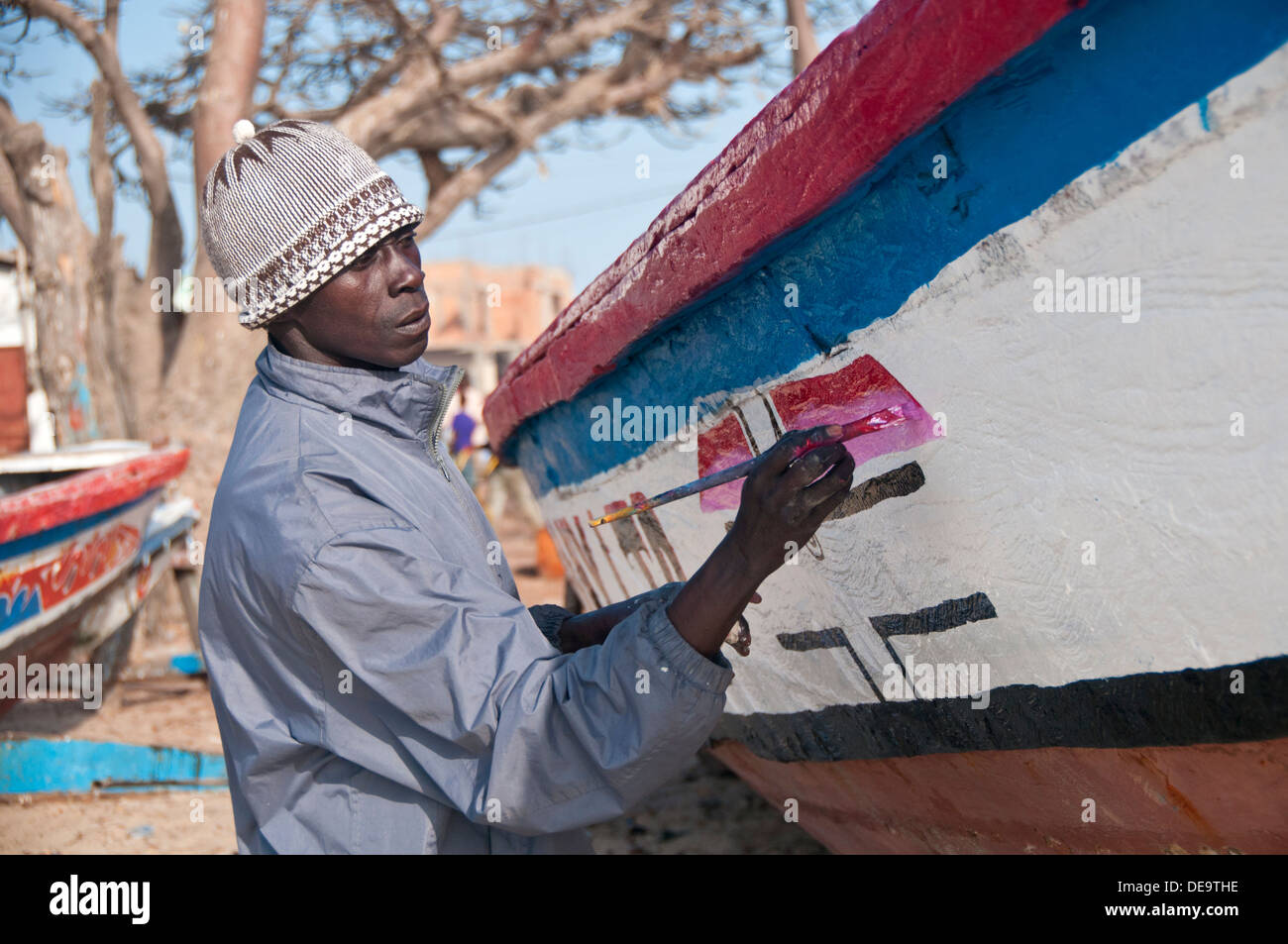 Local Gambian Man Painting Designs on Gambian Fishing Boat, Tanji, The Gambia, West Africa Stock Photo