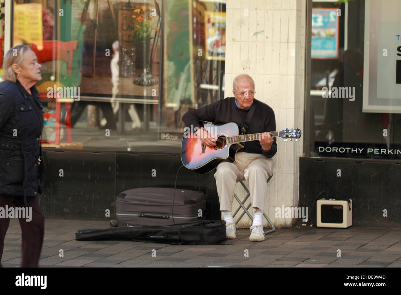 An elderly man busks in the street playing the acoustic guitar to crowds in Glasgow City Centre, Scotland, UK Stock Photo