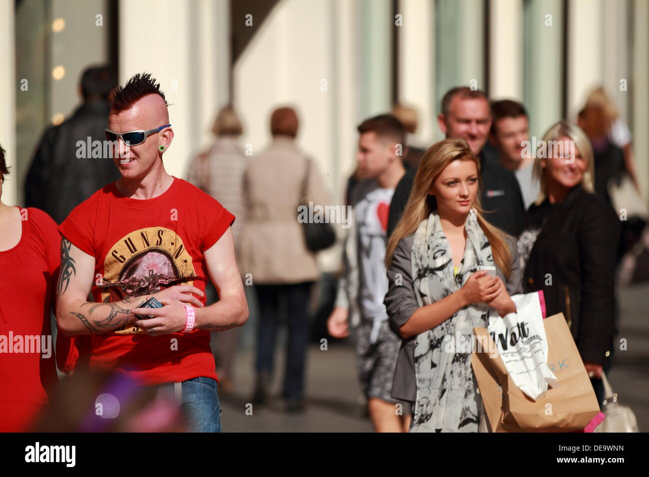 Man with spiky hair wearing sunglasses and sleeveless shirt and a woman with blonde hair watching buskers in Glasgow, Scotland, UK Stock Photo