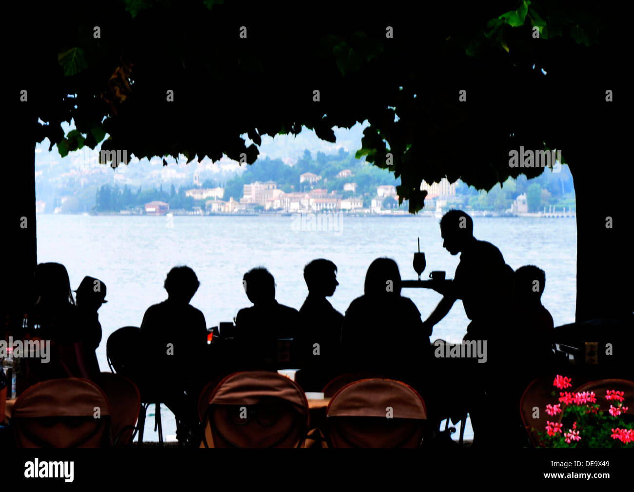 Italy - Lake Como - Bellagio - in silhouette - lakeside restaurant beneath trees - waiter serving customers at tables - outline Stock Photo