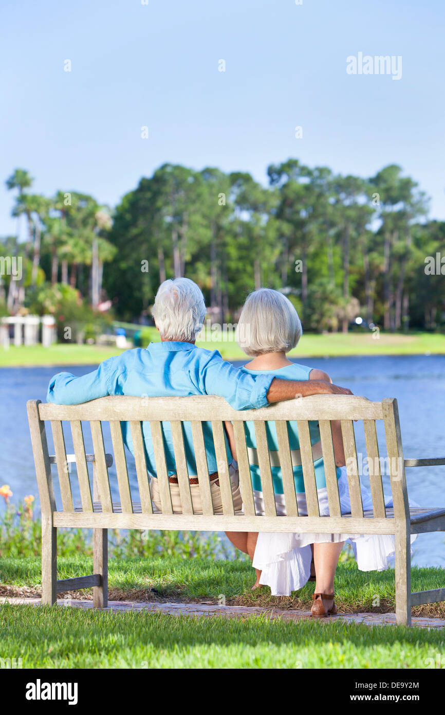 Rear view of a happy romantic senior couple sitting on a park bench ...