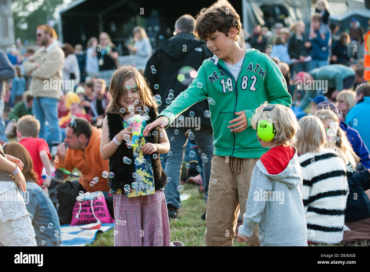 Happy young children play with a bubble machine in the crowd near the main stage at family friendly music festival Camp Bestival Stock Photo