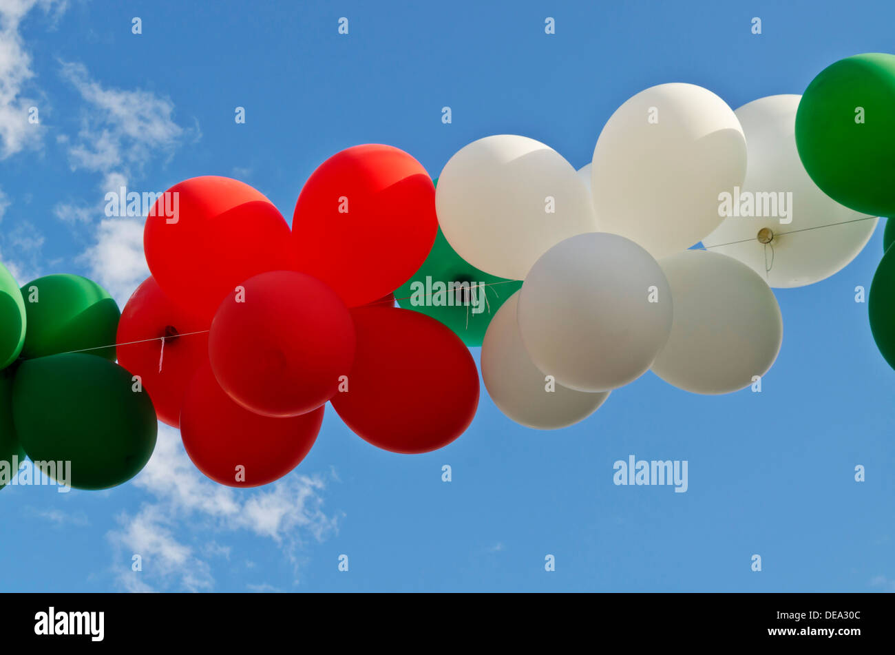 Colourful strand of red, white, and green balloons against a blue sky. Stock Photo