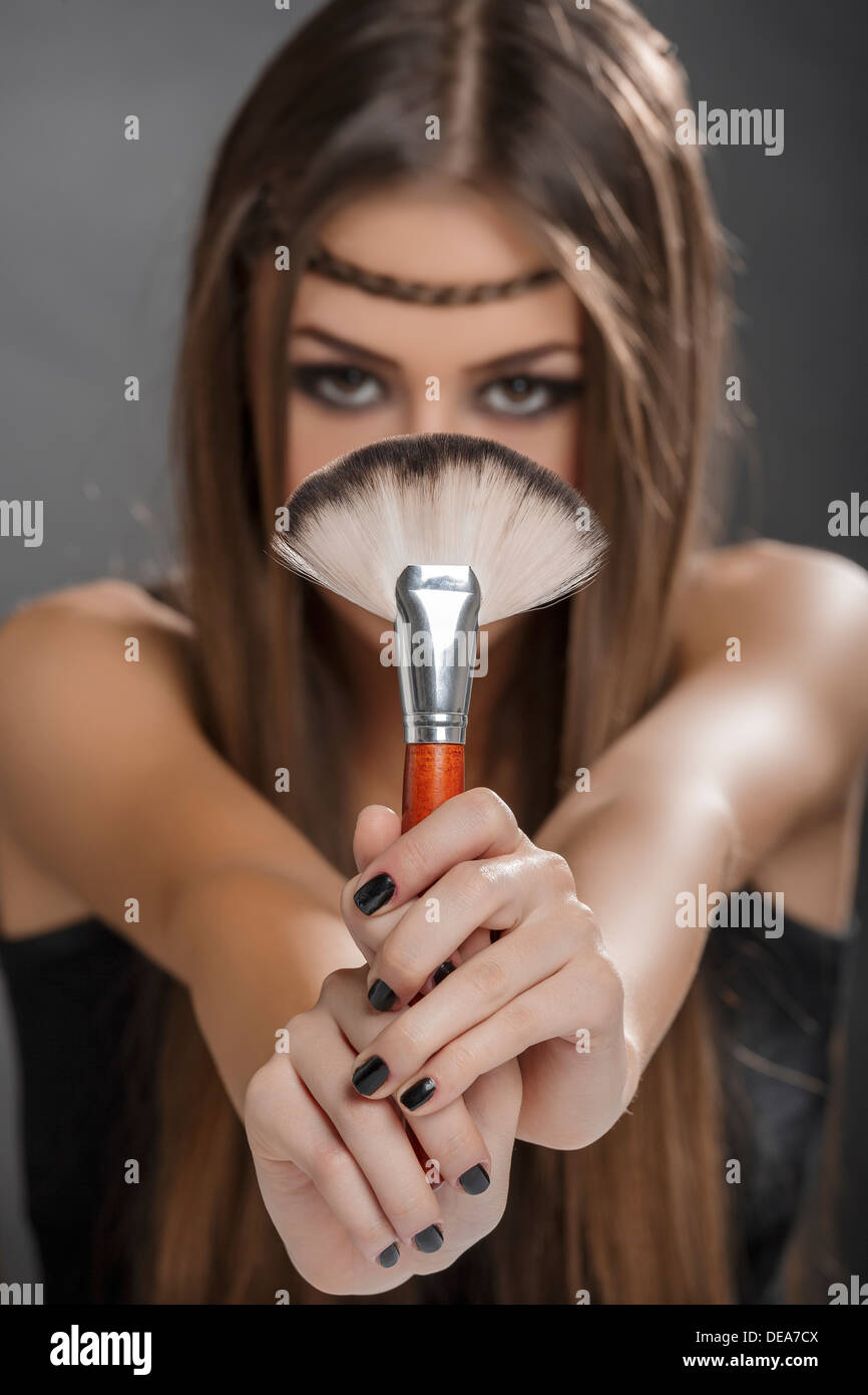 Young lady holding a big makeup brush with both hands in front of her