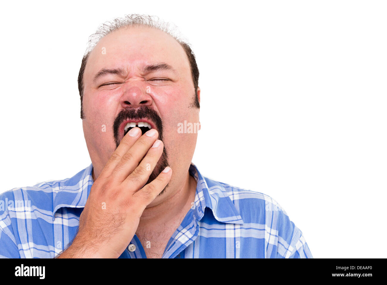 Tired man yawning with his hand to his mouth as he tries to fight off his exhaustion, isolated on white Stock Photo