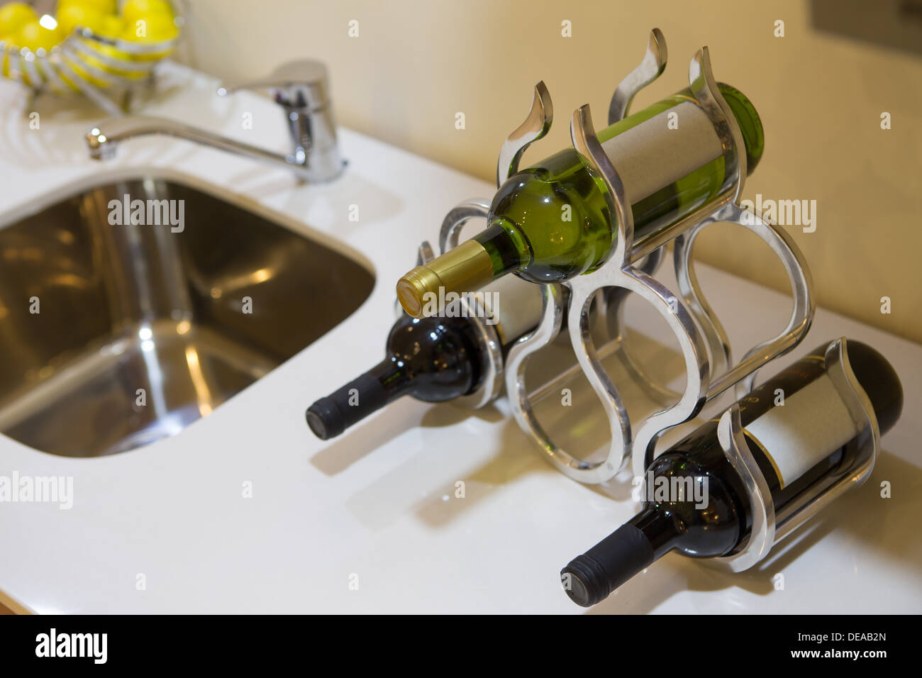 Three bottles of wine with blank labels in a stylish wine rack on a kitchen or bar counter alongside a sink Stock Photo