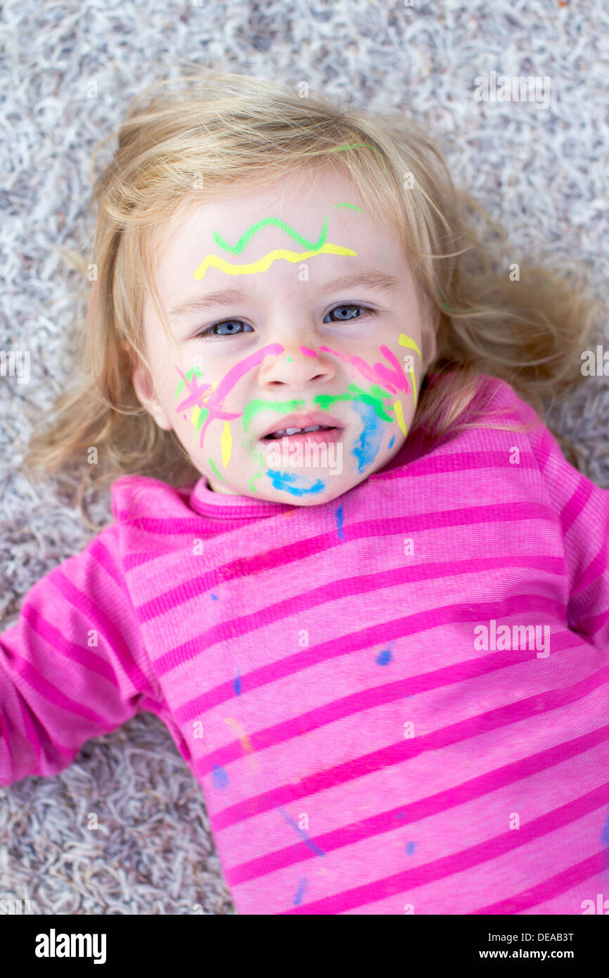 Child with paint on face lying on the floor Stock Photo