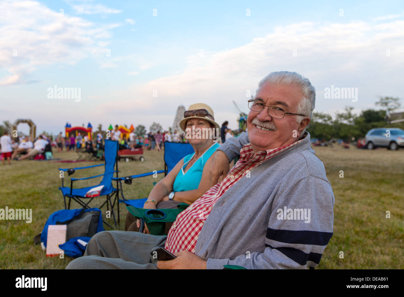 Elderly couple of spectators sitting in deckchairs at an outdoors event on a field turning to smile at the camera Stock Photo