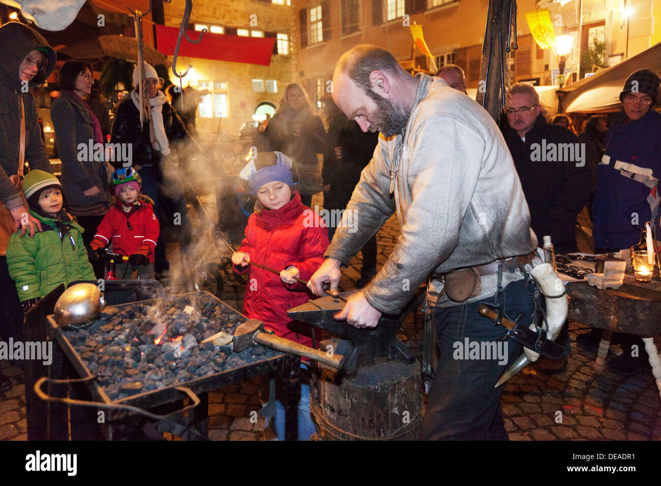 Six year old girl forges an amulet with the help of a blacksmith, Medieval Market, Christmas Fair, Esslingen, Germany Stock Photo