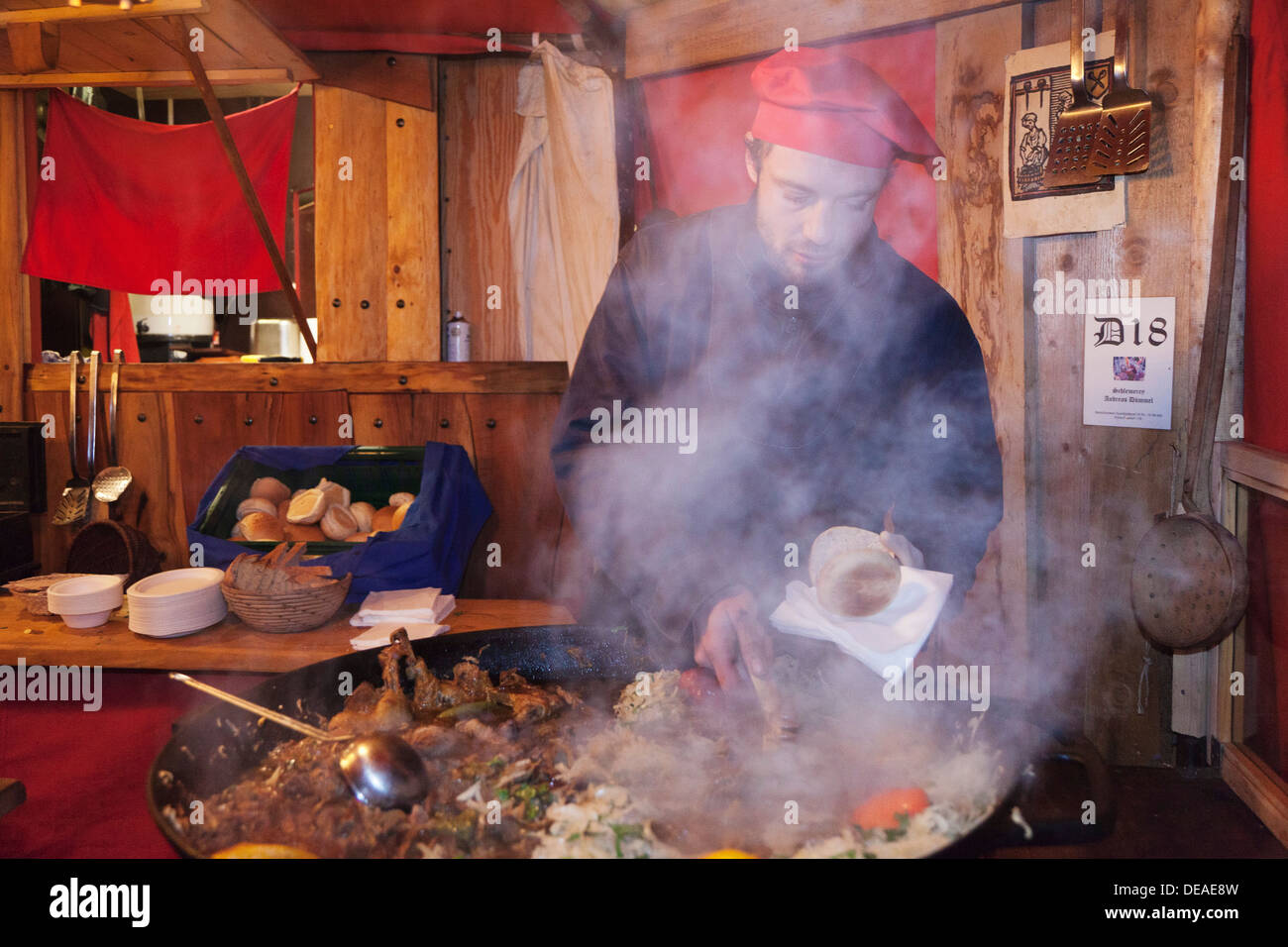 Young man at a stand cooking food at the Medieval market at the Christmas fair, Esslingen, Baden Wurttemberg, Germany Stock Photo
