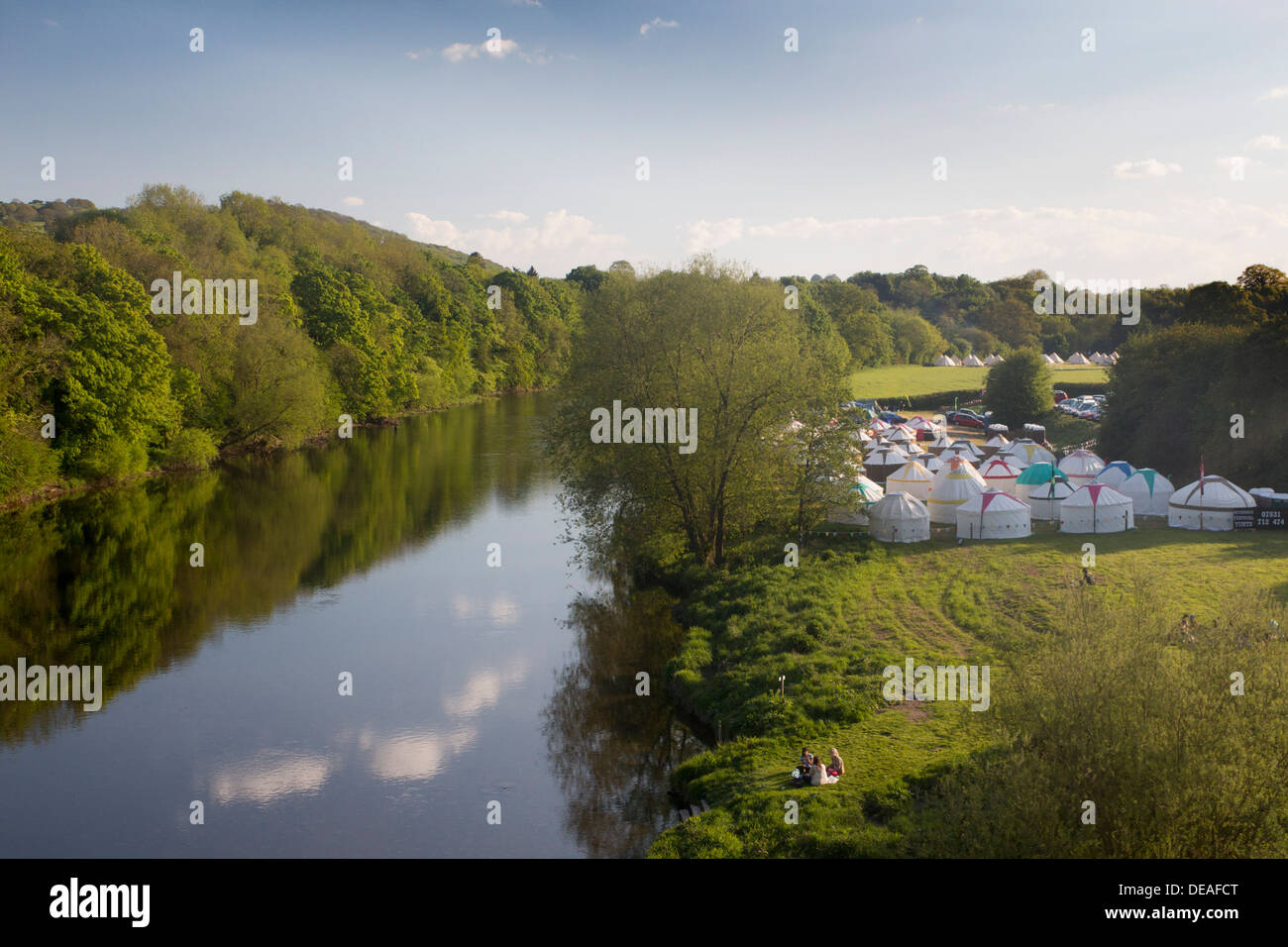 Yurts in field campsite by river Wye during festival Women sitting by river having picnic Hay-on-Wye Powys Wales UK Stock Photo