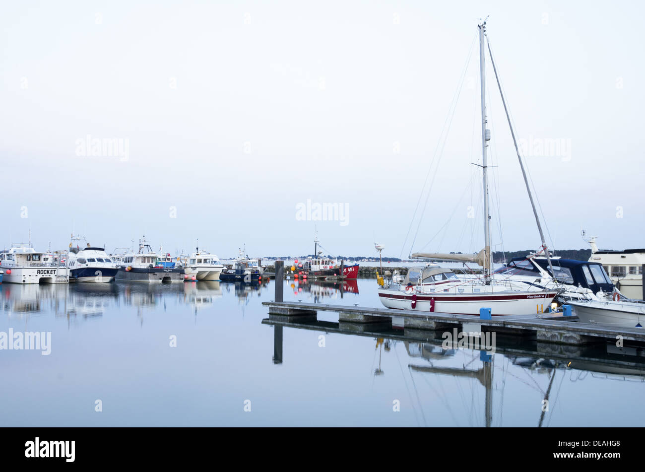 A view of Poole harbour with many boats and yachts on a calm late summer evening with perfect reflections in still water. Stock Photo