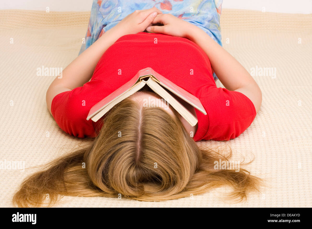 Girl, 17 years, lying on the floor covering her face with a book Stock Photo