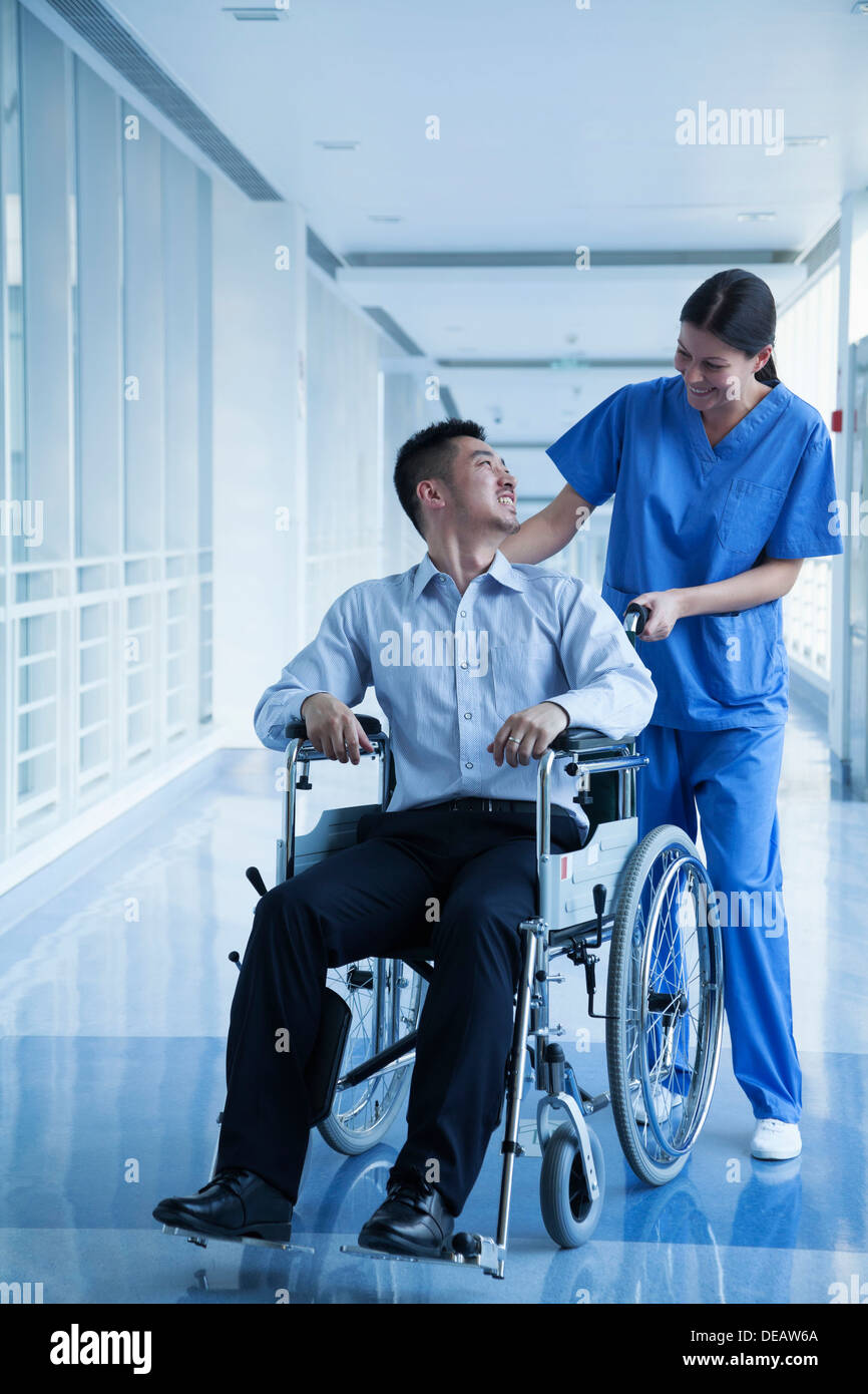 Smiling female nurse pushing and assisting patient in a wheelchair in ...