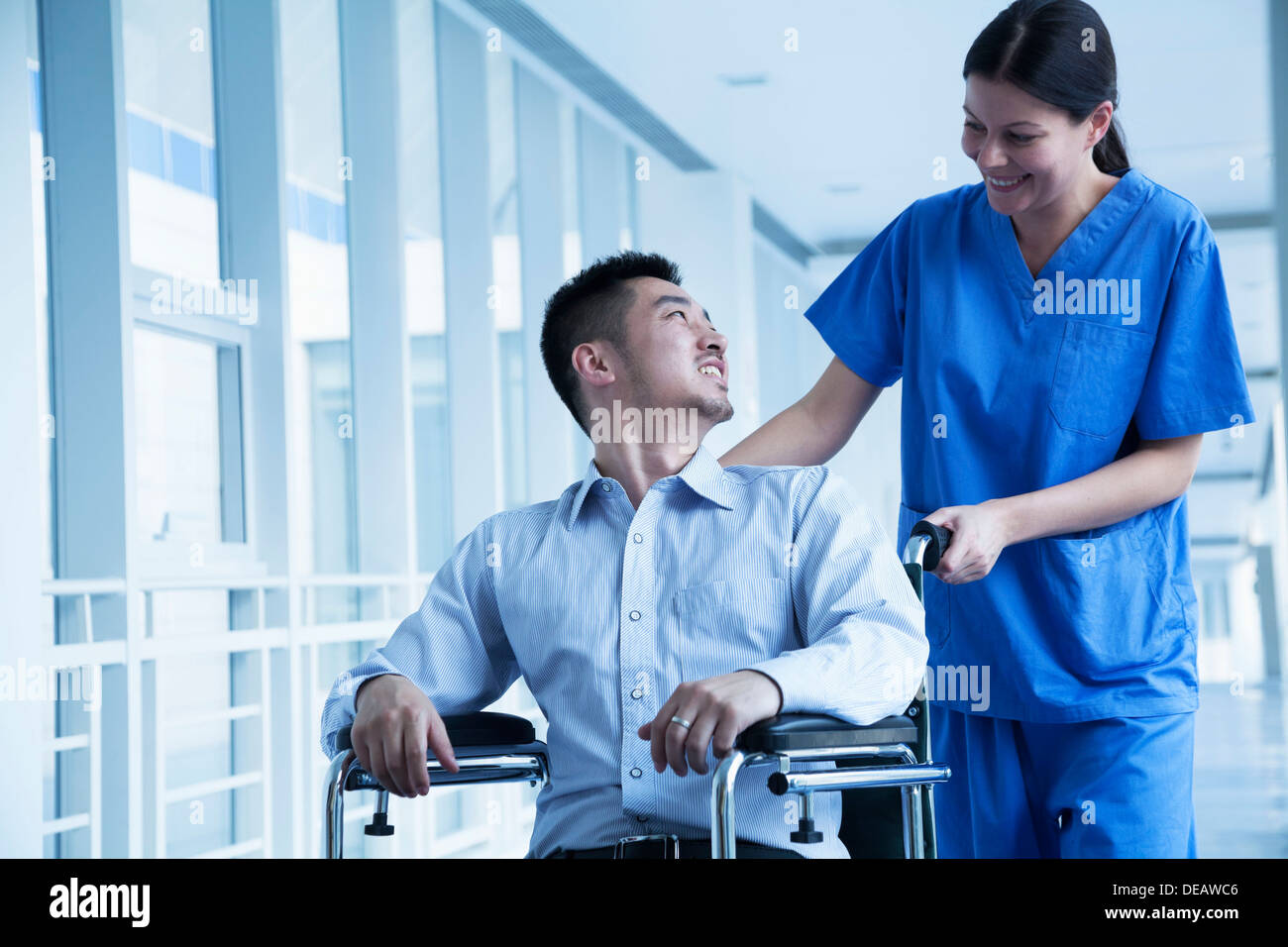 Smiling female nurse pushing and assisting patient in a wheelchair in ...