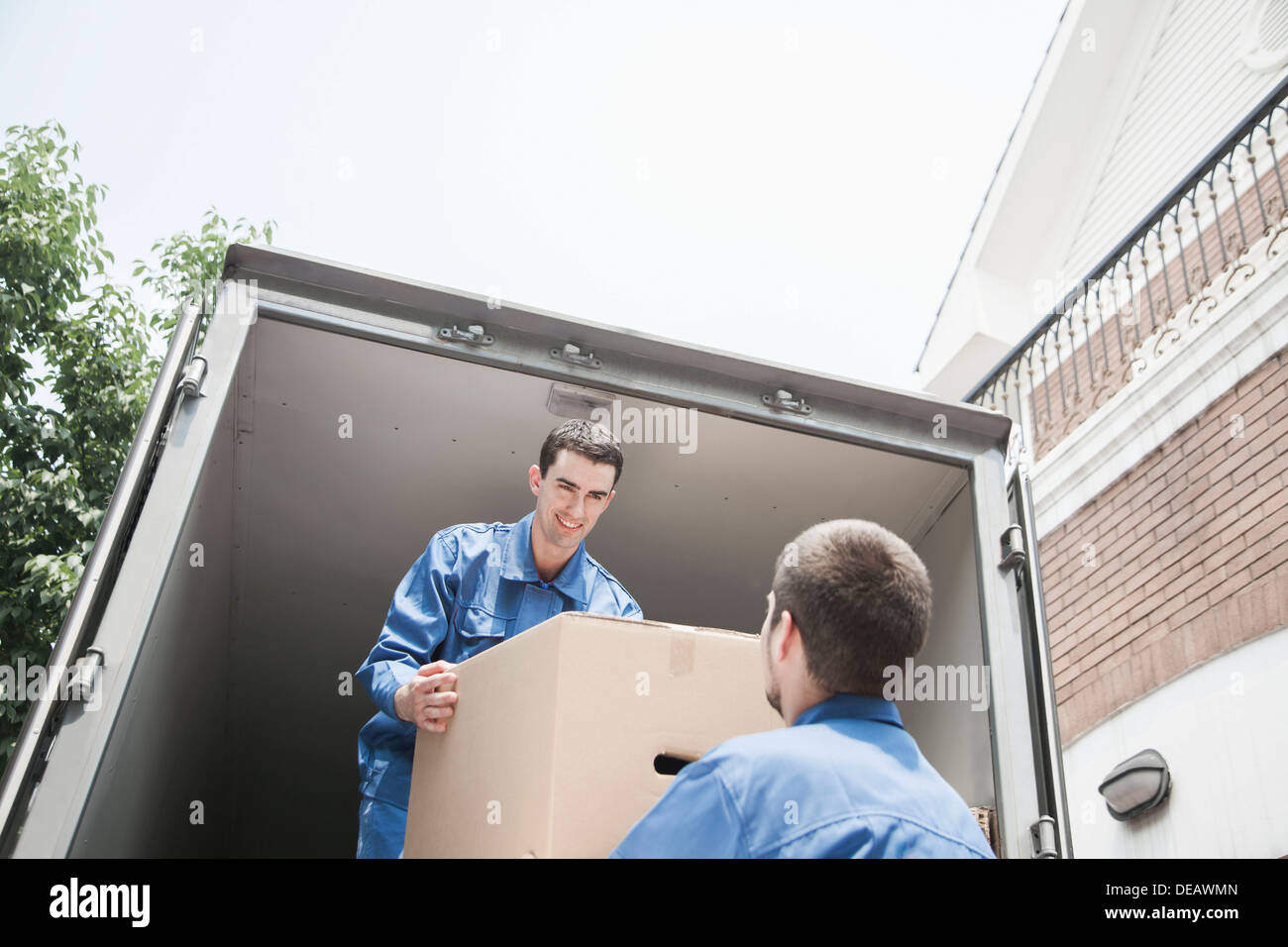 Movers unloading a moving van, passing a cardboard box Stock Photo