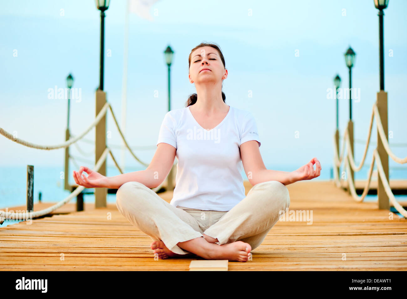woman dressed in white doing yoga on the pier near the sea Stock Photo