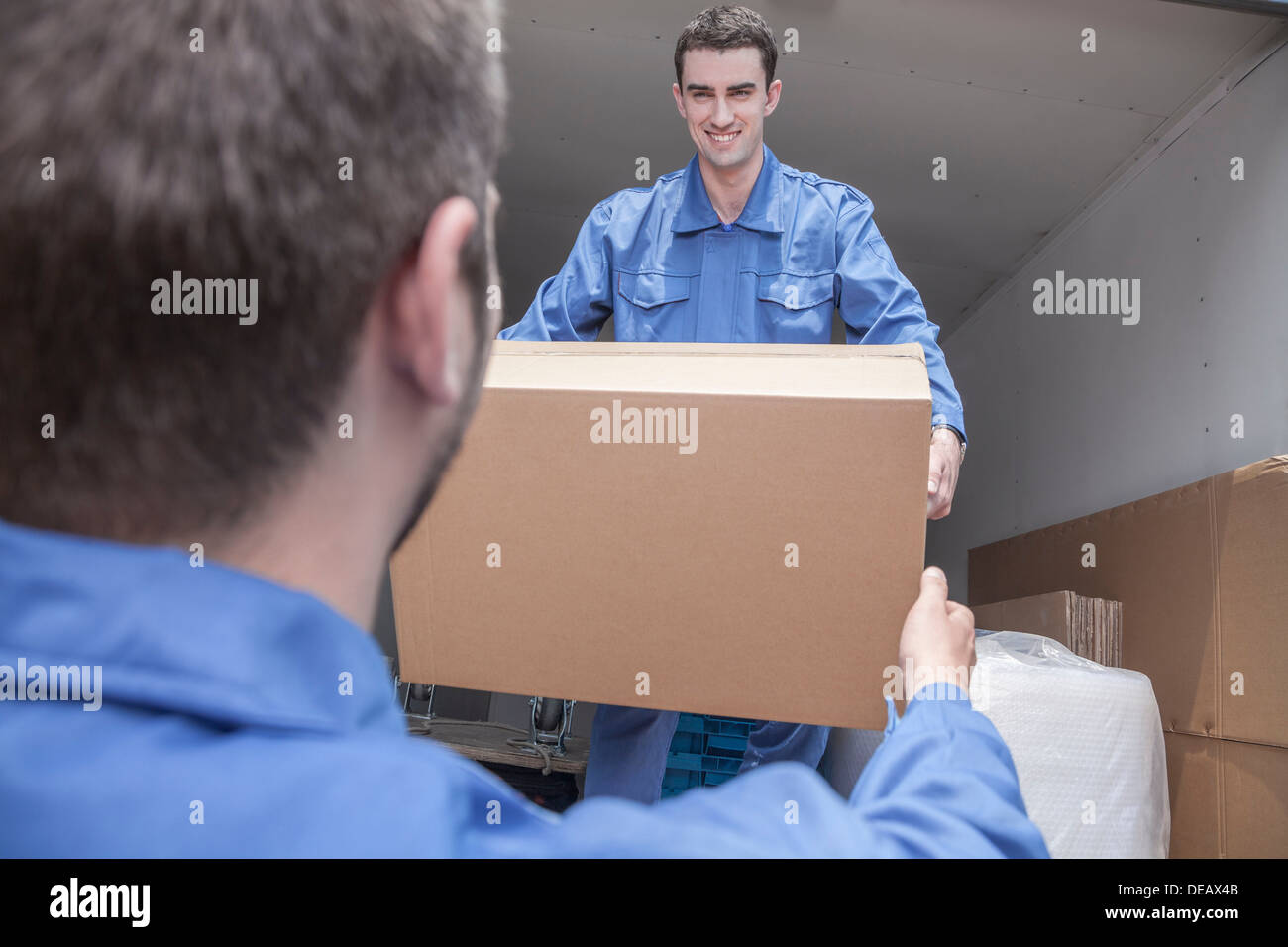 Movers unloading a moving van, passing a cardboard box Stock Photo