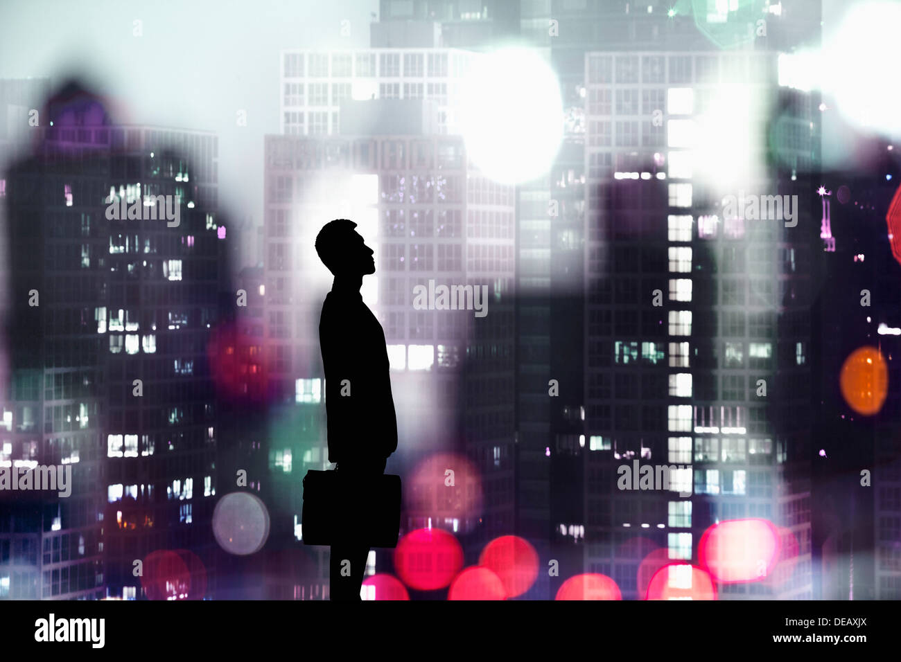 Silhouette of businessman holding a briefcase with a city at night time ...
