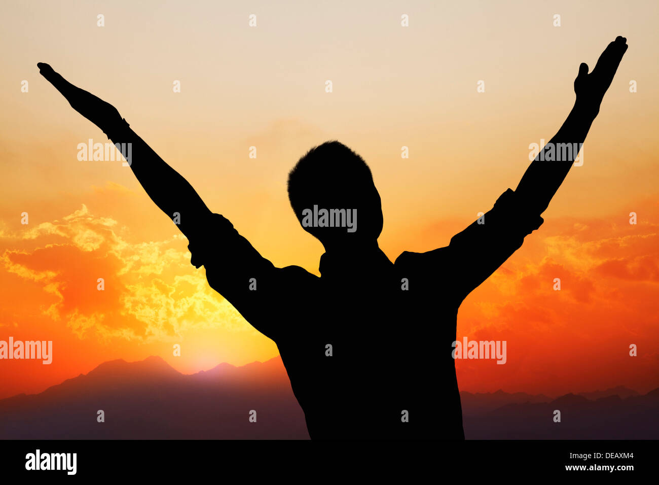 Silhouette of young man with arms raised with a beautiful sunset and ...