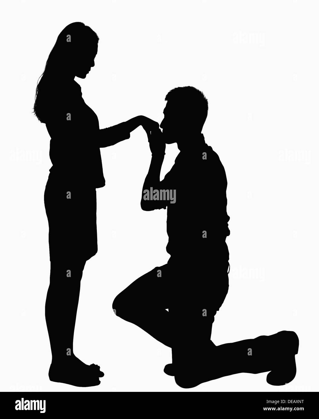 Silhouette of man on one knee, kissing woman's hand. Stock Photo