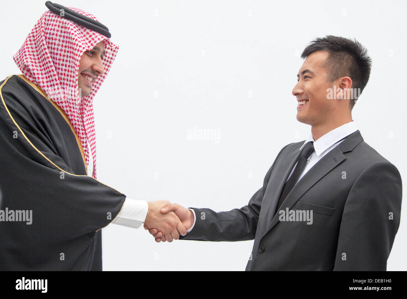 Smiling businessman and young man in traditional Arab clothing shaking hands, studio shot Stock Photo