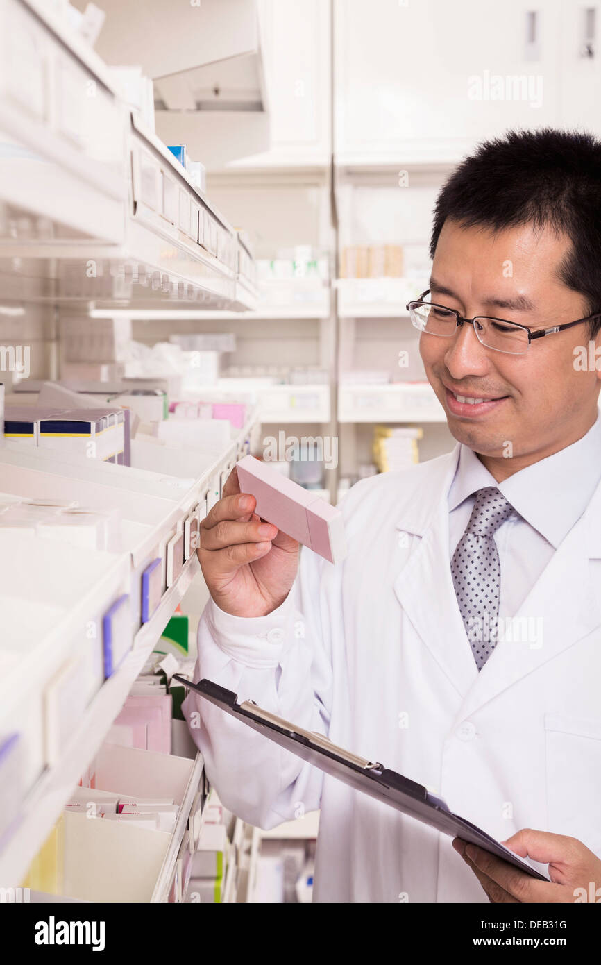Pharmacist taking down and examining prescription medication in a pharmacy Stock Photo