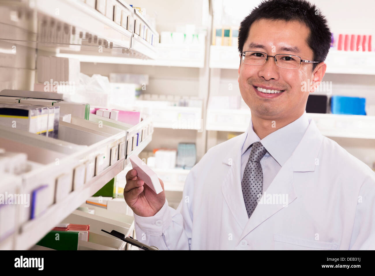 Pharmacist taking down and examining prescription medication in a pharmacy, looking at camera Stock Photo