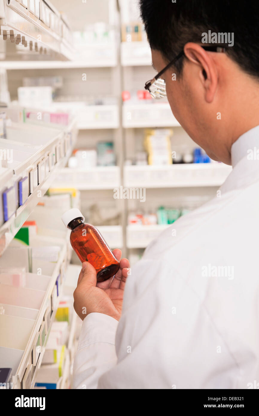 Pharmacist taking down and examining prescription medication in a pharmacy, rear view Stock Photo