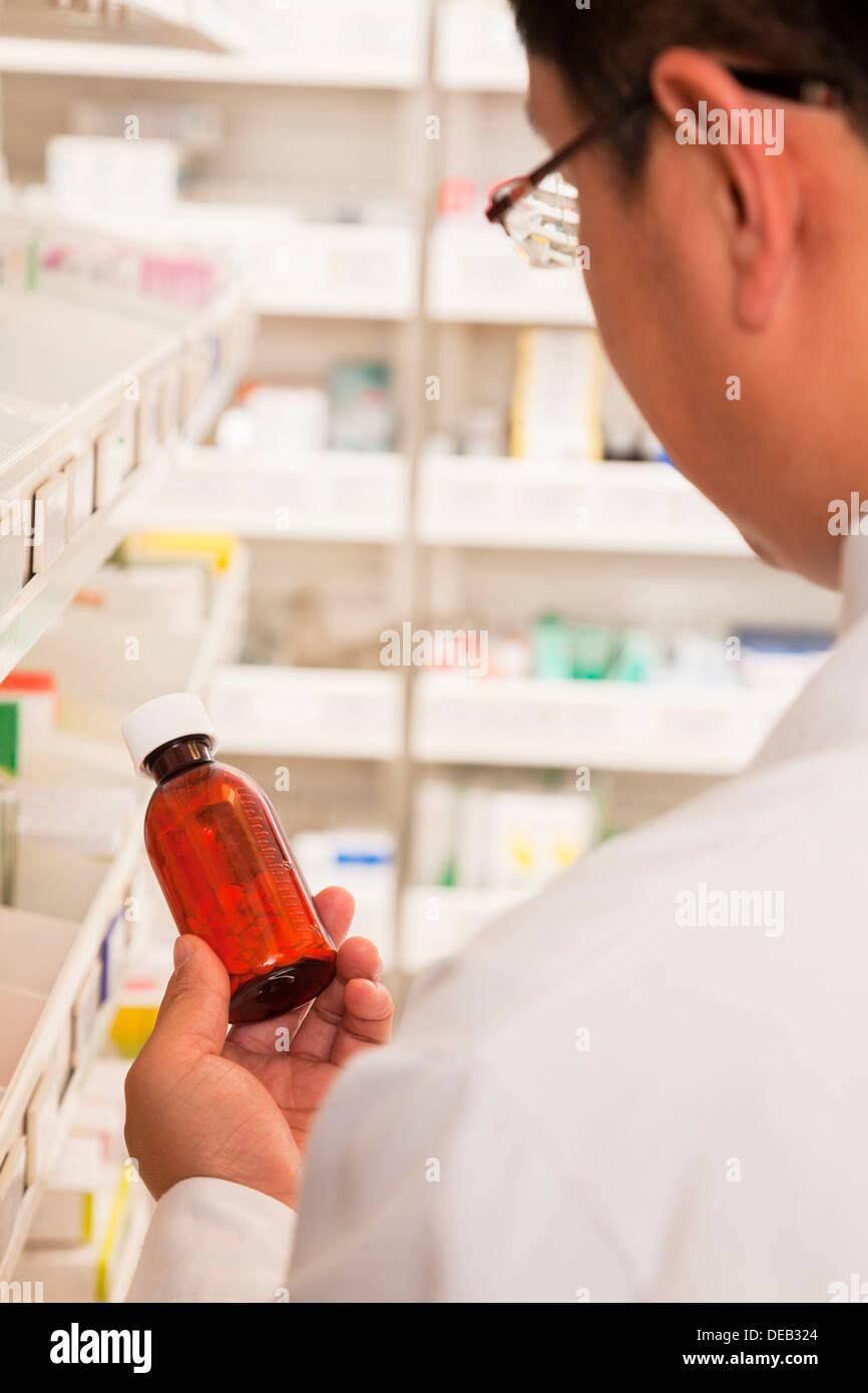 Pharmacist taking down and examining prescription medication in a pharmacy, rear view Stock Photo