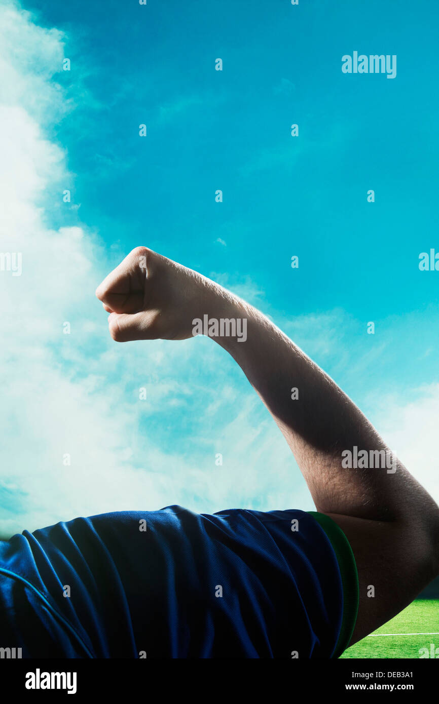 Soccer player flexing bicep during the day with sky in background Stock