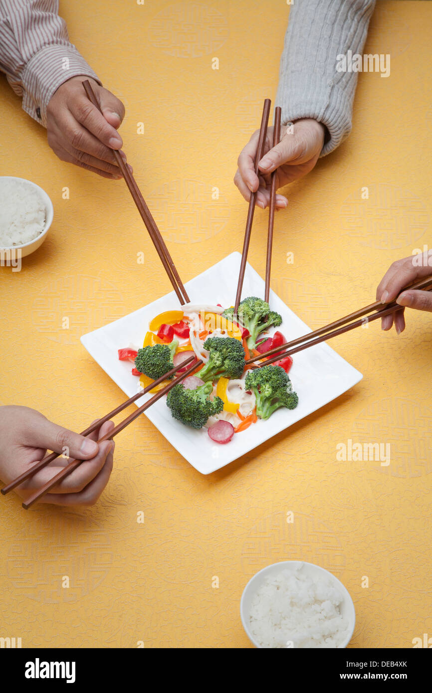 Close up of people holding chopsticks and sharing one dish Stock Photo