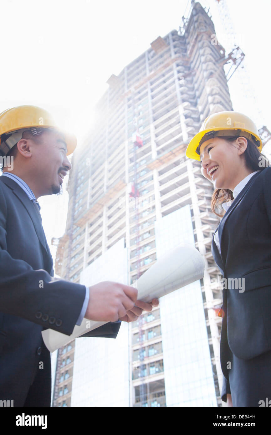 Two architects smiling at a construction site holding blueprint Stock Photo