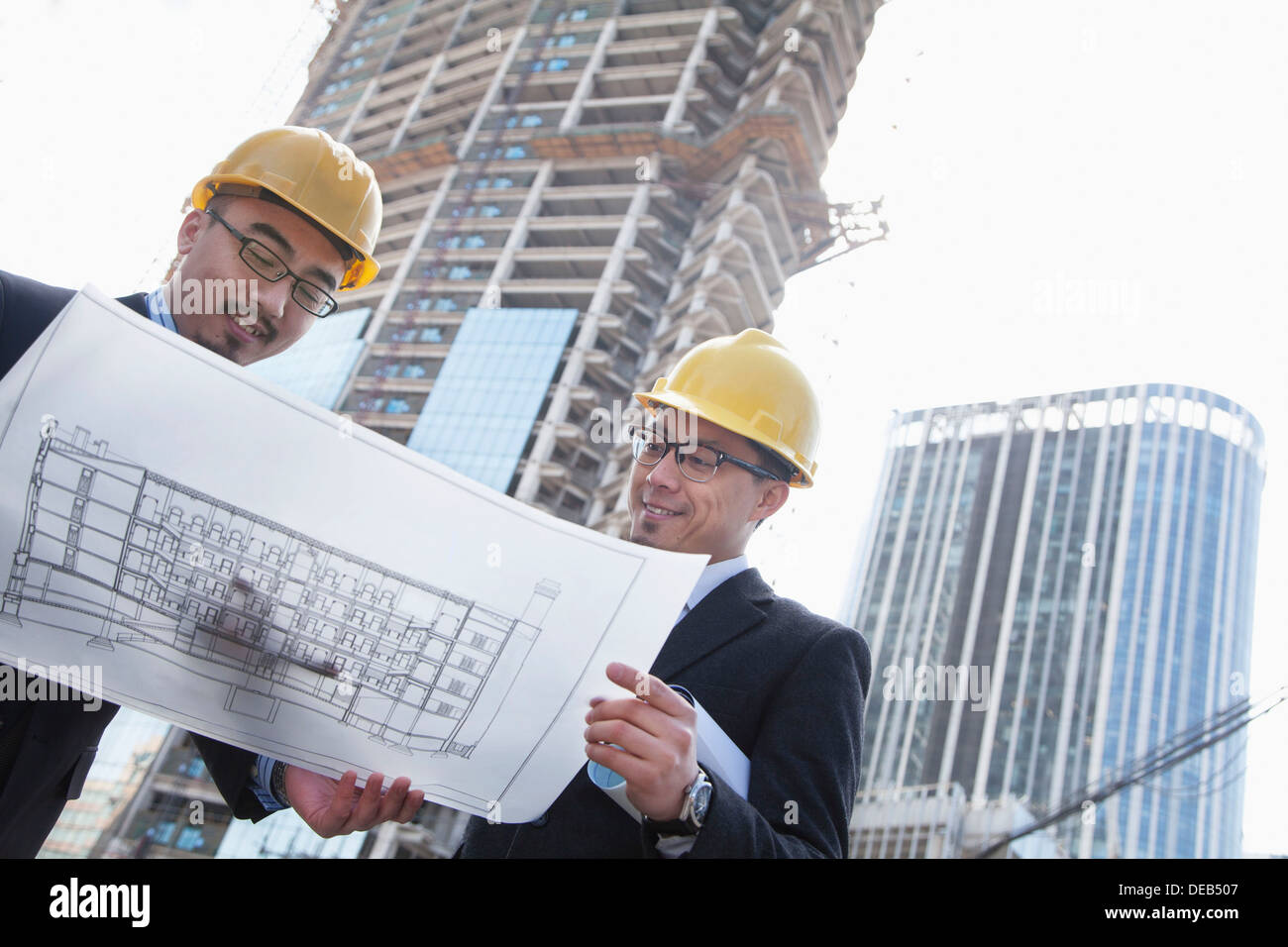 Architects looking at blueprint on construction site, Beijing Stock Photo