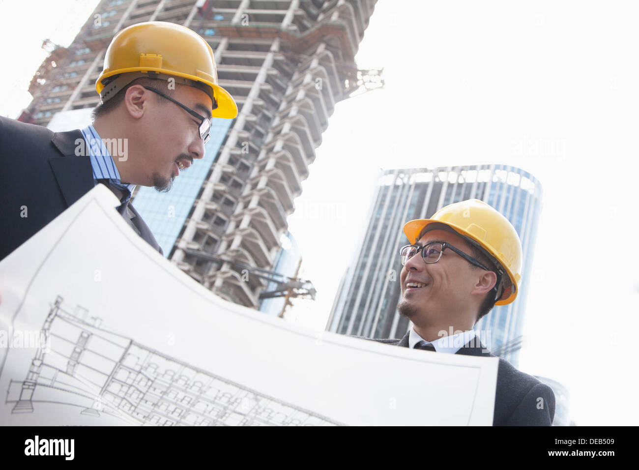 Architects looking at blueprint on construction site, Beijing Stock Photo