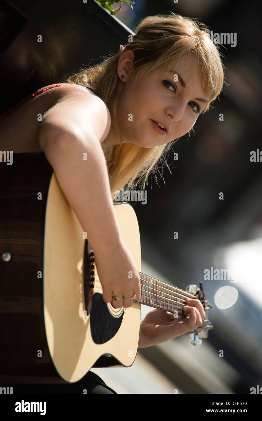 A young woman19 year old teenage girl playing acoustic guitar busking on  the street on a hot summer morning UK Stock Photo - Alamy