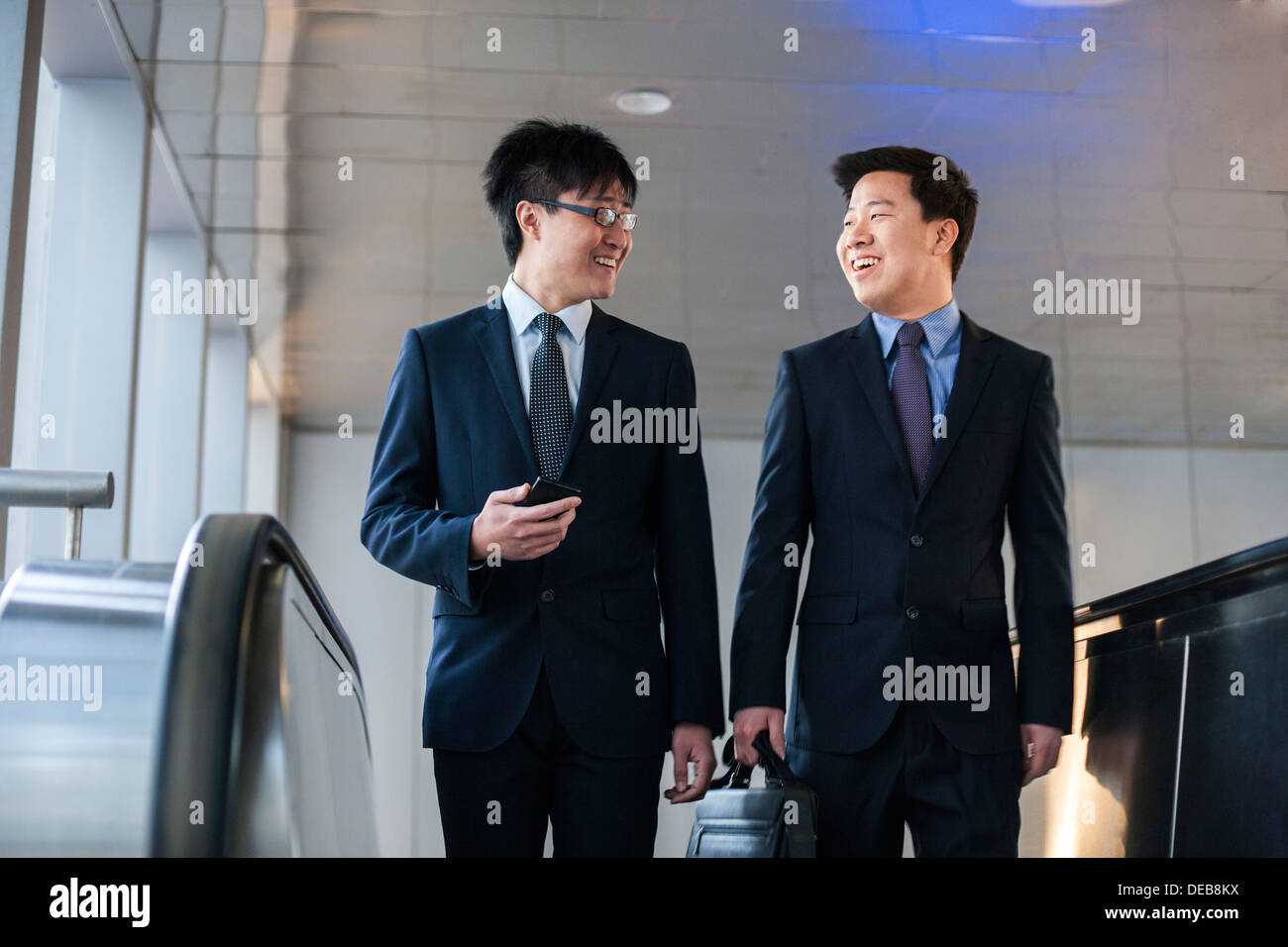 Two smiling businessmen coming up the escalator together Stock Photo