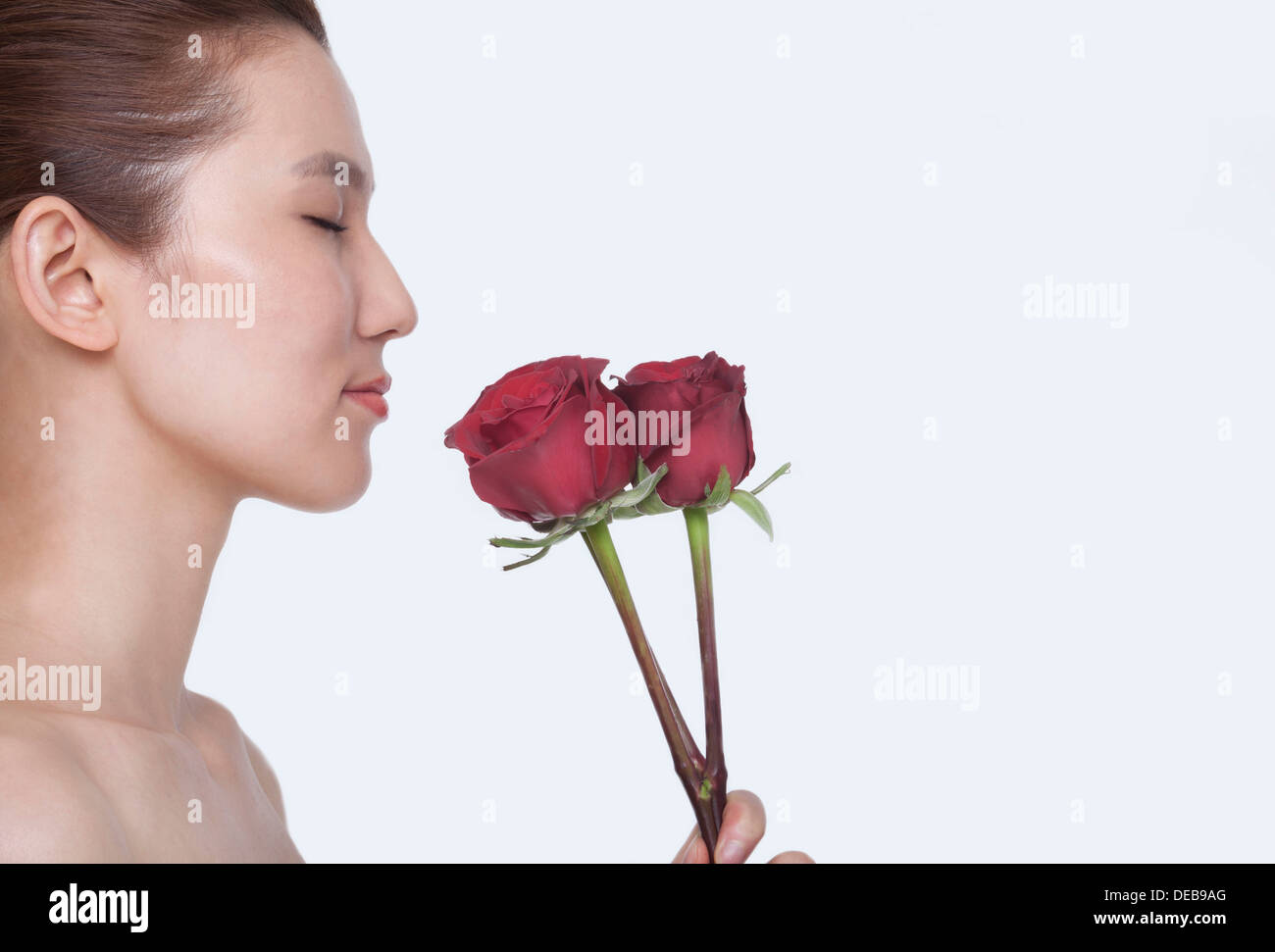 Beautiful young woman with eyes closed smelling a red rose, studio shot ...