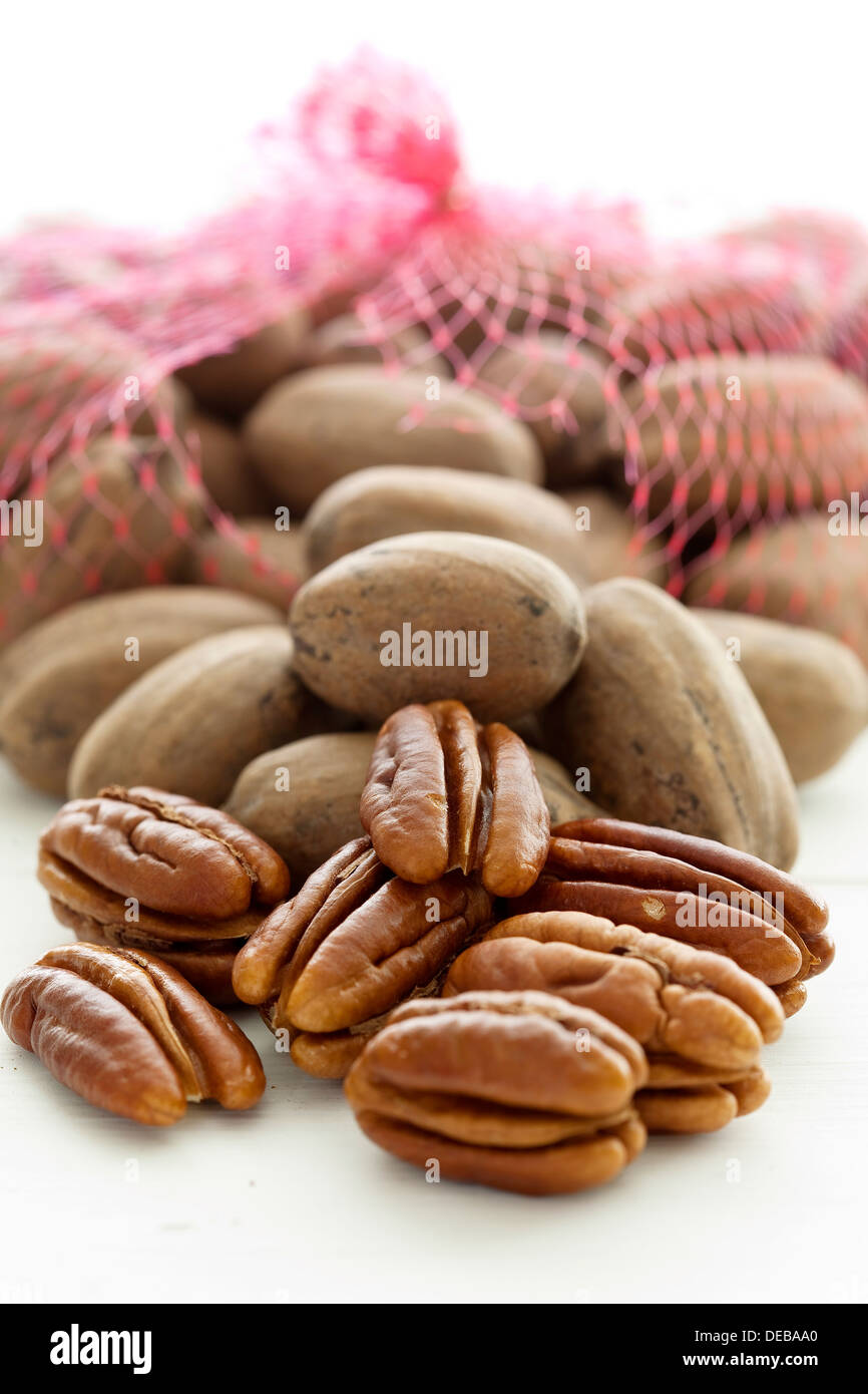Shelled pecan nuts in front of a netted bag of unshelled pecans on a white background. Stock Photo