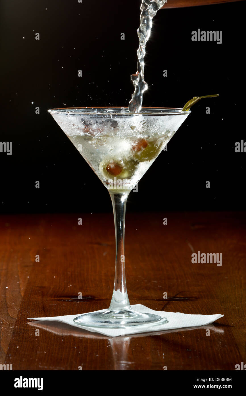 dirty vodka martini splashing into a cocktail glass with green olives Stock Photo