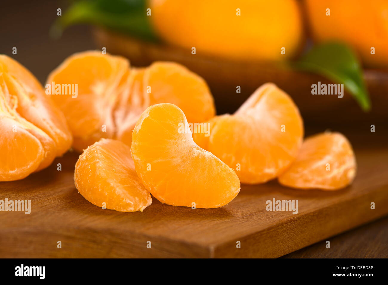 Mandarin segments on wooden board with mandarins in the back (Selective Focus, Focus on the front of the first mandarin segment) Stock Photo